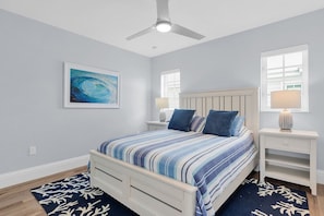 A bedroom with a bed, a ceiling fan, a nightstand, a lamp, a framed picture, and a window. - Beach Walk to Sombrero (Marathon)