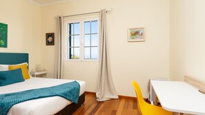 A hotel room with a bed, a desk, a chair, a window with curtains, and a picture on the wall. - Desertas Vista Casa by LovelyStay (Gaula)