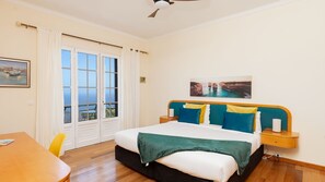 A hotel room with a bed, a desk, a chair, a window with curtains, a ceiling fan, and artwork on the walls. - Desertas Vista Casa by LovelyStay (Gaula)