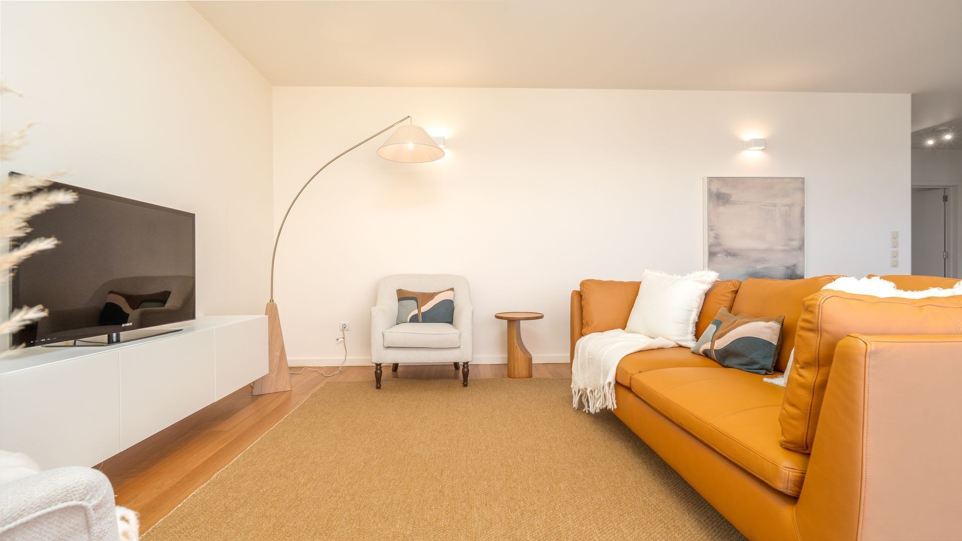 Un salon moderne comprenant un téléviseur à écran plat, un canapé, un fauteuil, une lampe sur pied et une petite table d’appoint.