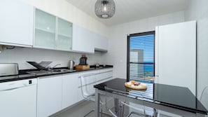 Eine moderne Küche mit weißen Schränken, einem Geschirrspüler von Bosch, einer Kaffeemaschine und einem Fenster mit Jalousien.