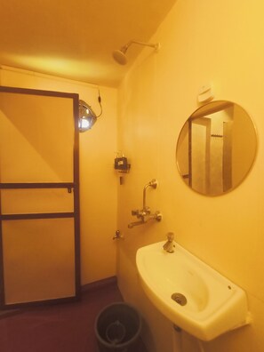 Un bagno con lavandino, specchio, doccia e cestino.