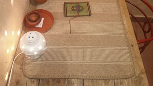 A small, cozy room with a woven mat, a small table with a decorative plate, a clay pot, and a small wooden box. - Shades of Kashi with an artistic and cozy stays for couple and family. (varanasi)