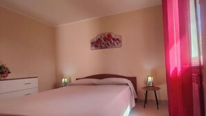 Un dormitorio con cama, mesitas de noche, cómoda, un adorno en la pared y una ventana con cortinas.