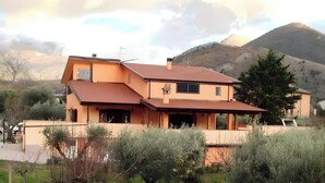 Ein zweistöckiges Haus mit geneigtem Dach, einer überdachten Veranda und einem Berg im Hintergrund.