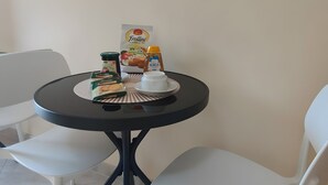 Uma área de refeições com uma mesa redonda, duas cadeiras brancas e uma pequena mesa branca com comida e uma xícara de café.