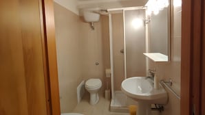 A bathroom with a toilet, bidet, sink, and shower.