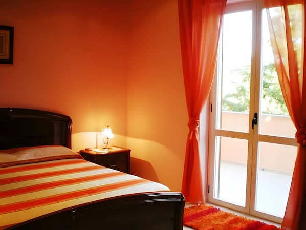 Ein Zimmer mit einem Bett, einem Nachttisch mit Lampe und einem Fenster mit Vorhängen.