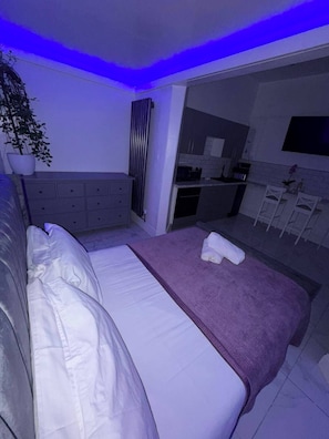 A modern bedroom with a bed, a dresser, and a small kitchenette.