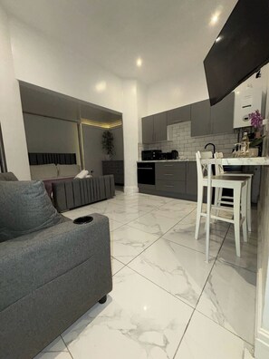 A modern kitchen with a dining area, a grey sofa, and a white chair.