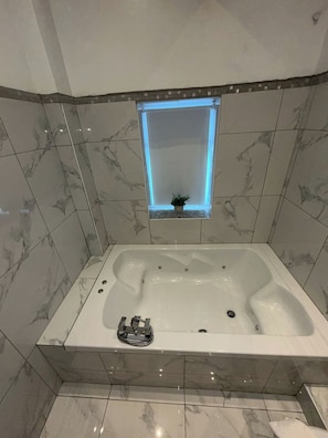 A modern bathroom with a large bathtub, a small window with a plant, and marble tiles.