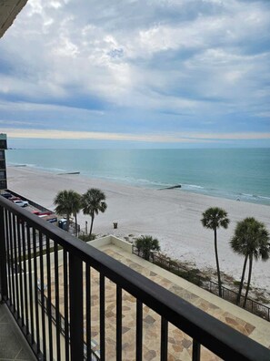 Blick auf einen Strand von einem Balkon mit Geländer, Palmen und blauem Himmel.