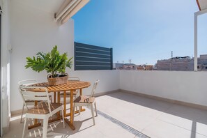 A balcony with a wooden table and chairs, a potted plant, and a view of buildings in the background. - 2-bedroom Apartment in Guargacho, Tenerife sur (Arona)