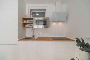 Eine kleine Küche mit integriertem Mikrowellenherd, Spüle und einer Holzausziehtafel.