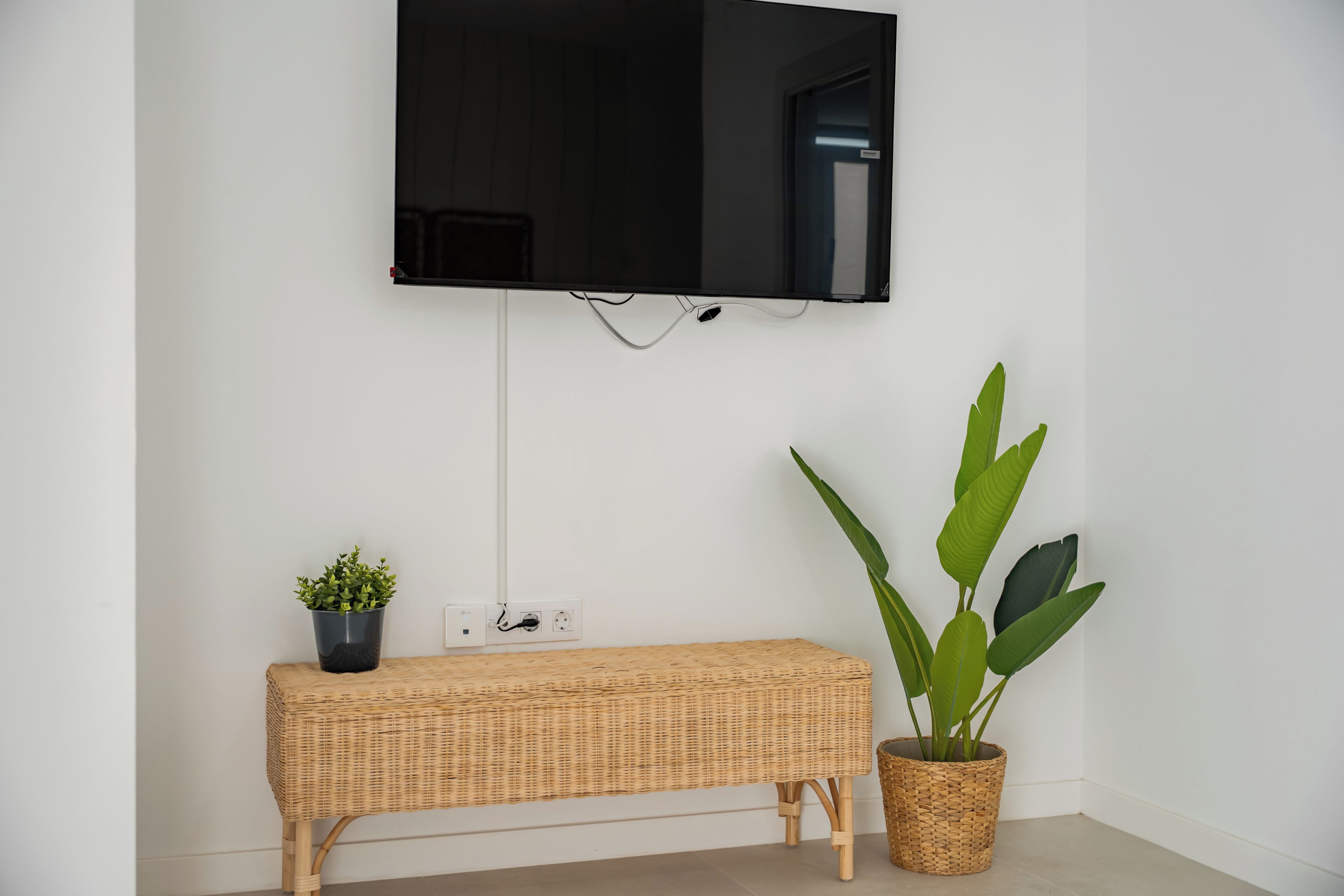 Una TV a parete sopra una panca in vimini con una pianta in vaso accanto.
