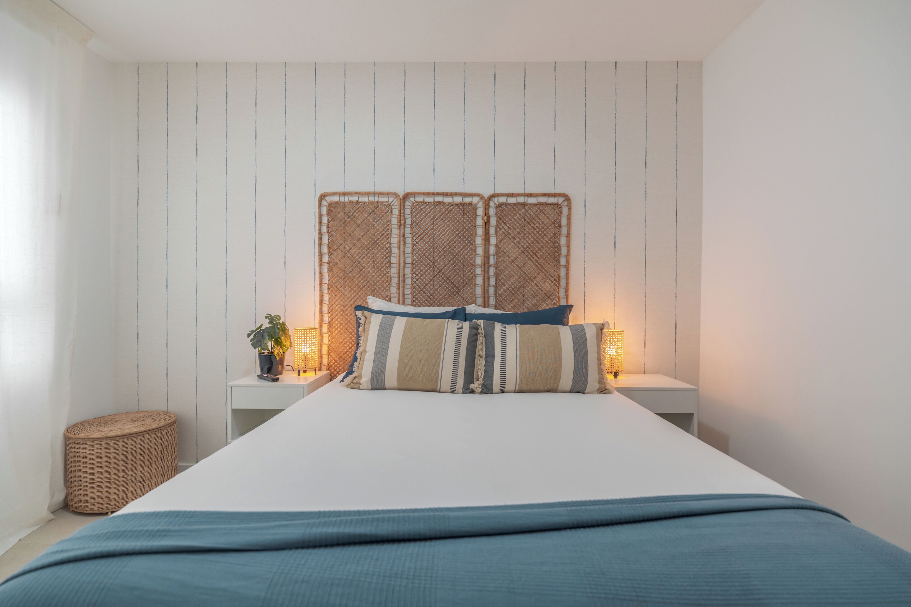 A bedroom with a bed, a bedside table with a lamp, and a small wicker stool.