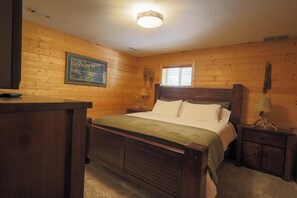 Een slaapkamer met houten lambrisering, een bed, nachtkastjes, een lamp en een lijst met een foto aan de muur.