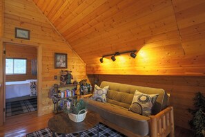 A cozy cabin interior with a wooden ceiling, a sofa with patterned cushions, a coffee table, and a bookshelf with various items. - Luxury Cottage w/NEW HOT TUB near National Parks and Loaded with Amenities (Duck Creek Village)