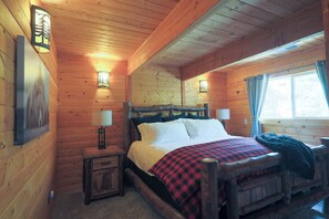 Ein Zimmer in einer Holzhütte mit einem Bett, zwei Nachttischen und einem mit Vorhängen versehenen Fenster.