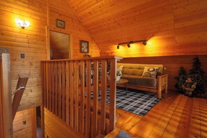 A cozy cabin interior with a wooden staircase, a sofa, a small table, and a Christmas tree. - Luxury Cottage w/NEW HOT TUB near National Parks and Loaded with Amenities (Duck Creek Village)