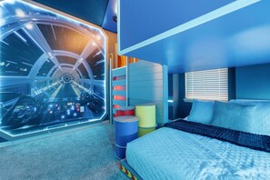 Ein Schlafzimmer mit Bett, Fenster mit Jalousien, einem wandmontierten Fernseher und einem großen Fenster mit Blick auf einen Raum im Weltraum-Design.