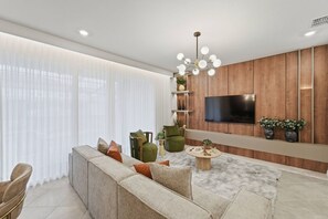 Ein modernes Wohnzimmer mit einer Couch, Sesseln, einem Couchtisch, einem Fernseher und einer Wand als Holzdekor.