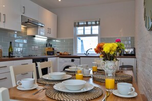 Eine moderne Küche mit weißen Schränken, einem eingebauten Ofen und einer Essecke mit einem Holztisch, gedeckt für das Frühstück.