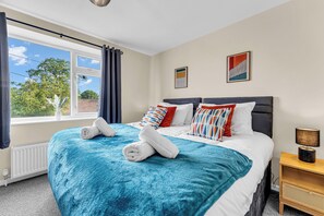 A bedroom with a large bed, a window with curtains, a radiator, and a bedside table with a lamp. - Haregate House | 3BR Leek | Peak District | Sleeps 5 (Leek)
