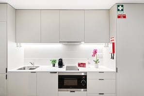 Eine moderne Küche mit weißen Schränken, einer Edelstahl-Spüle, einer Mikrowelle und einem kleinen Topfpflanzen.