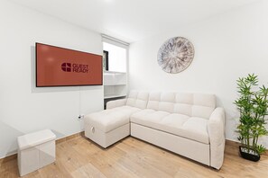 Una sala de estar moderna con un sofá seccional color beige, una mesita auxiliar blanca, un televisor montado en la pared, un adorno circular decorativo y una planta en maceta.