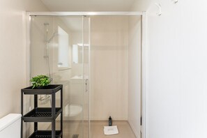 Un baño moderno con cabina de ducha de vidrio, un estante negro con artículos de aseo y un letrero en el suelo que dice 'GUEST READY'.