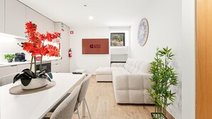 Ein modernes Wohnzimmer mit einem weißen Sofa, einem Esstisch mit Stühlen, einer Küchenzeile und einem großen Fenster.