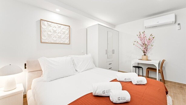 Ein Hotelzimmer mit Bett, Schreibtisch, Stuhl, Kleiderschrank und Wandklimaanlage.