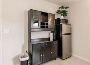Eine Küchenzeile mit Mikrowelle, Kühlschrank, dunklen Schränken und einem Mülleimer.