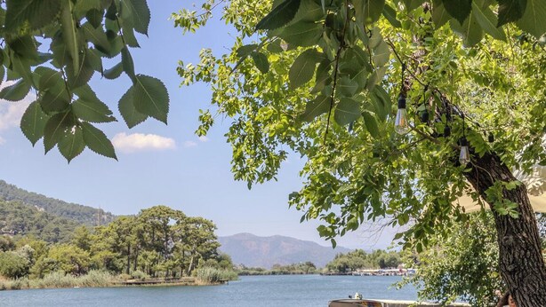 A lakeside dining area with tables set for two, overlooking a calm lake and distant mountains. - Aydos Hotels & Breeze Restaurant (Ortaca)