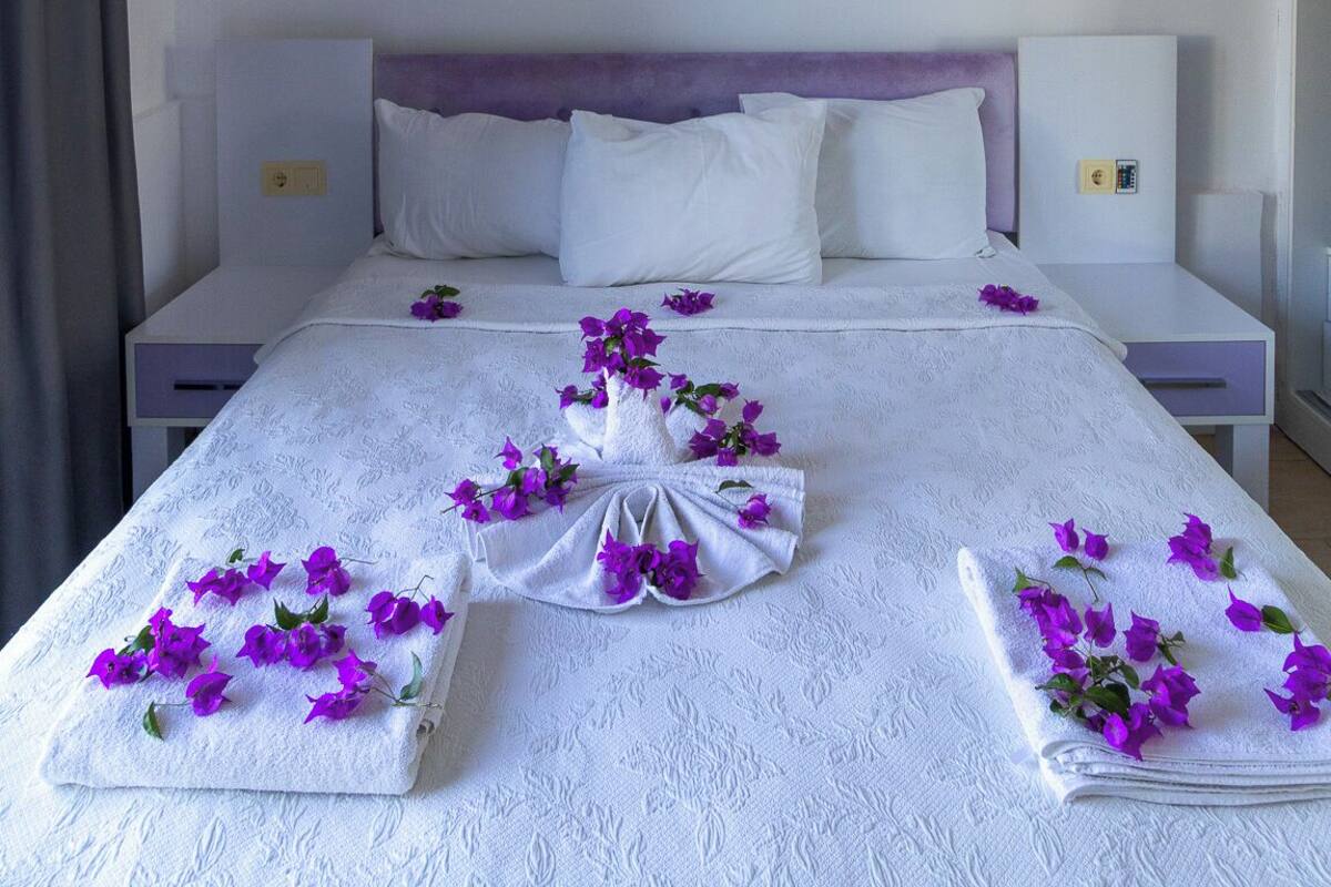 A hotel room with a neatly made bed, a wall-mounted air conditioner, and a bedside table with a lamp.