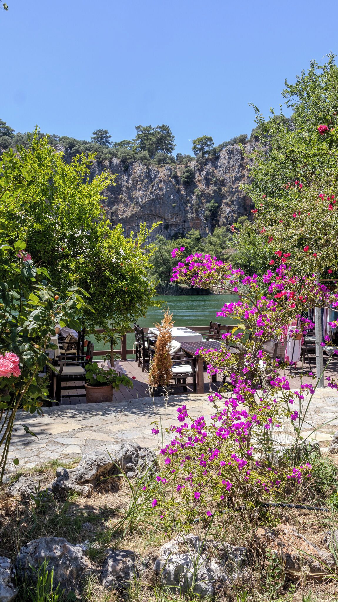 A patio with outdoor seating, a view of a lake, and a rocky cliff in the background.