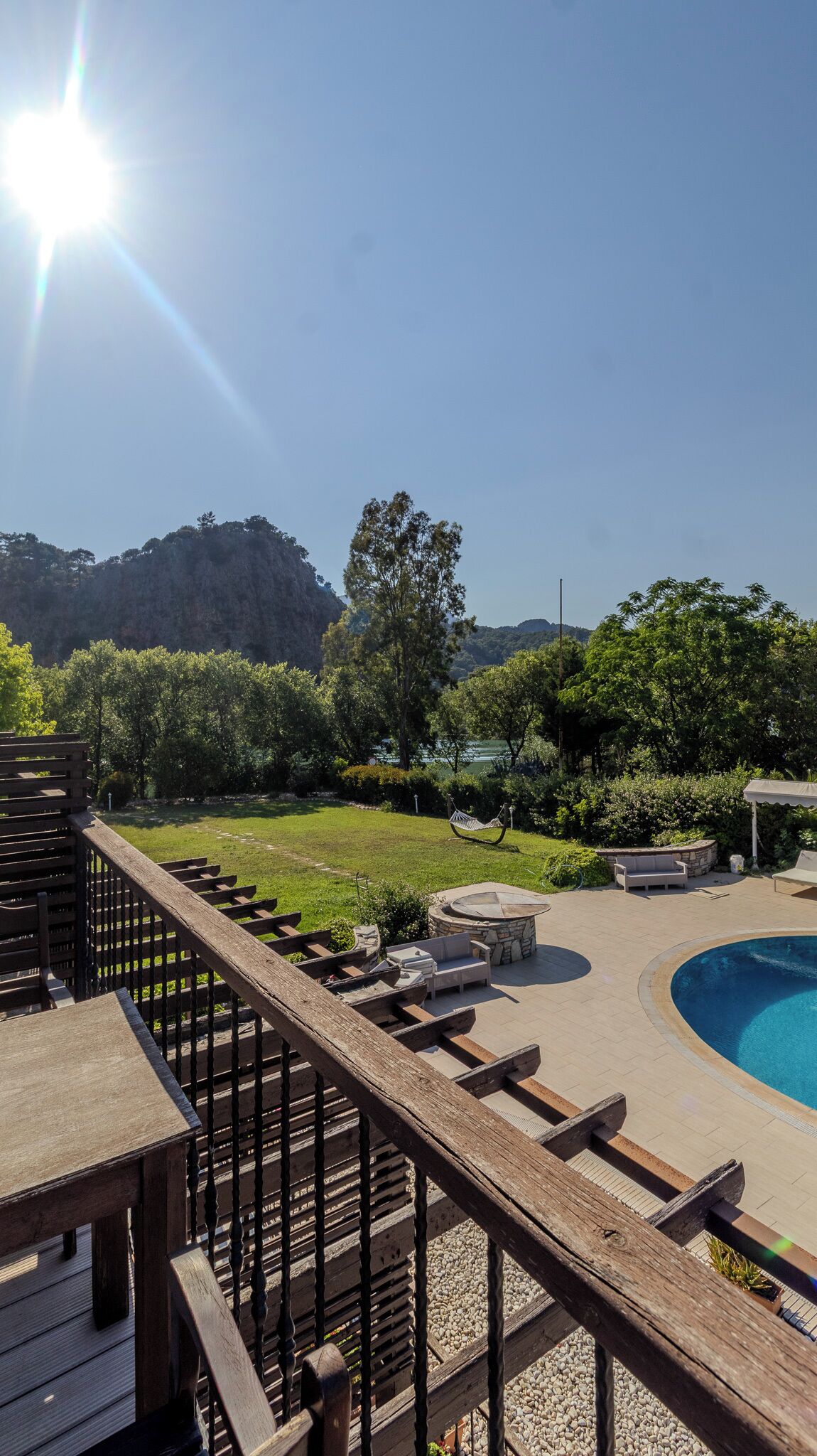 A poolside area with a wooden deck, seating, and a view of a mountain.