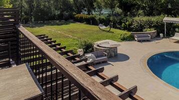 A poolside area with a wooden deck, seating, and a view of a mountain.