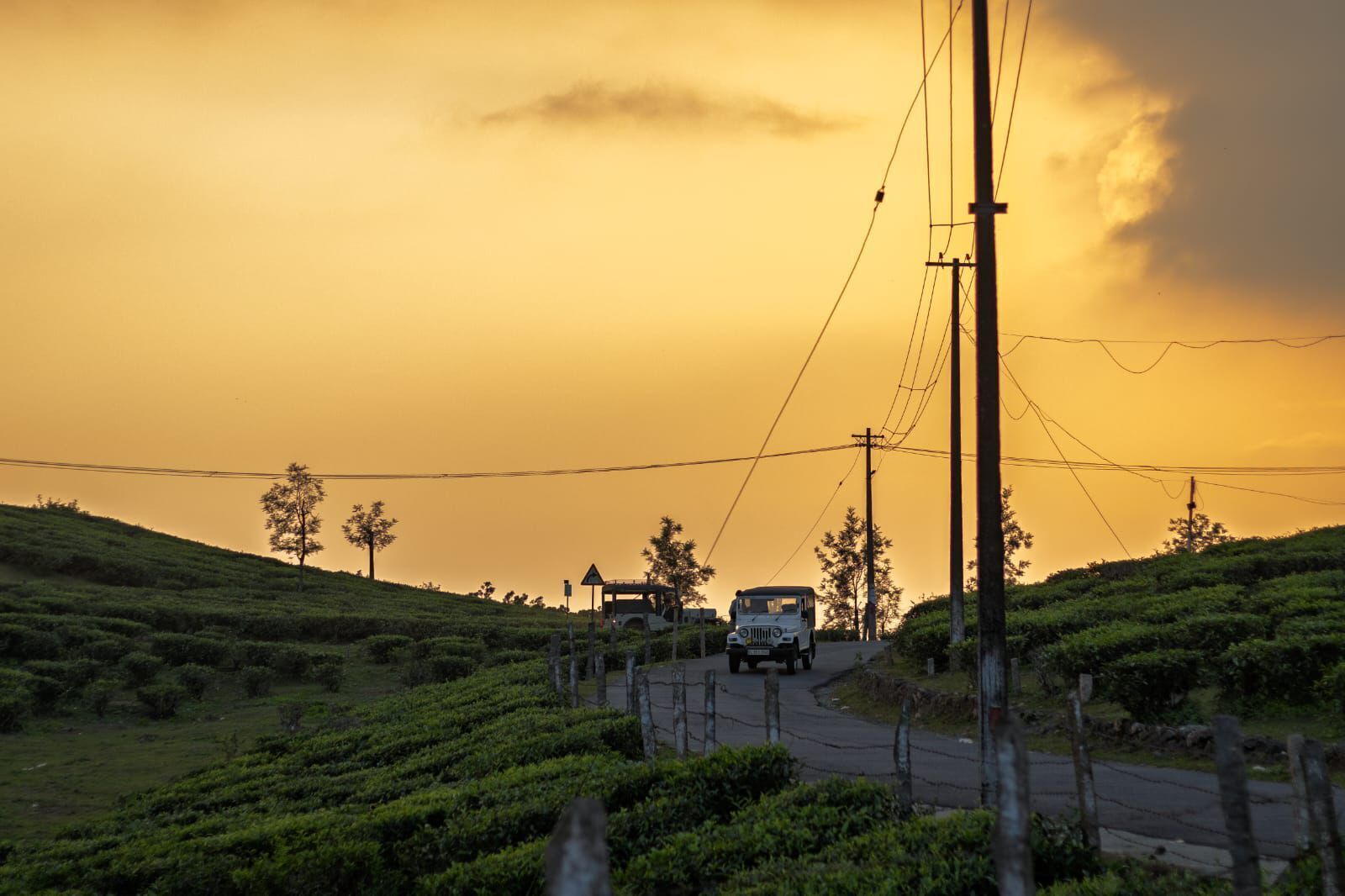 Uma estrada rural com um veículo, rodeada por vegetação e linhas de energia.