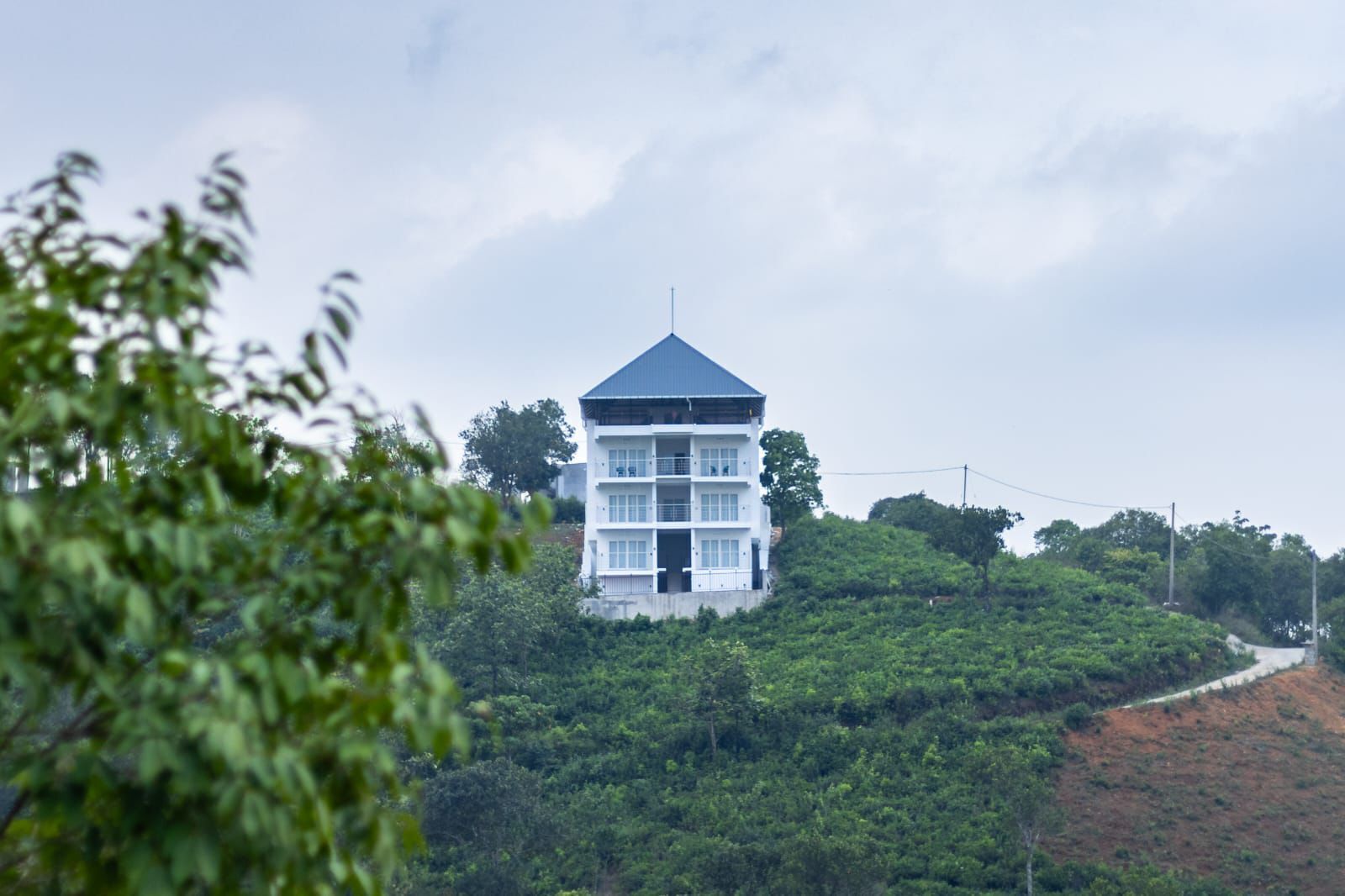 A multi-story building with a flat roof, surrounded by lush greenery and a hilly landscape.