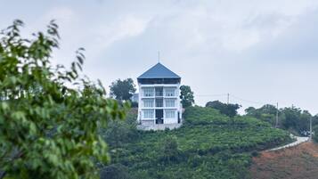 A multi-story building with a flat roof, surrounded by lush greenery and a hilly landscape.
