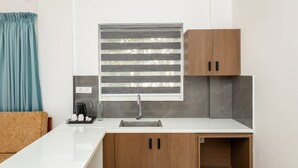 Una cocina moderna con encimera blanca, un fregadero, armarios de madera y una ventana con persianas.