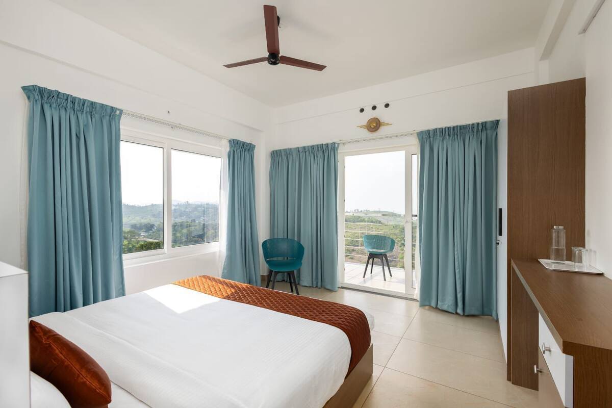 A hotel room with a bed, a desk, a chair, and a balcony with a view.