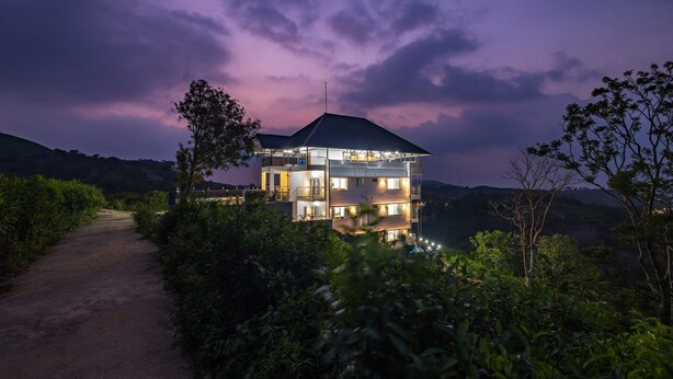 A multi-story building with a balcony, surrounded by greenery and a dirt path. - Nithara Hills Resort (Peermade)