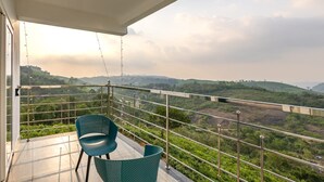 A balcony with two chairs, a view of green hills, and a cloudy sky. - Nithara Hills Resort (Peermade)