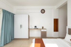 A hotel room with a bed, a desk with a coffee maker, a clock, and a wardrobe. - Nithara Hills Resort (Peermade)