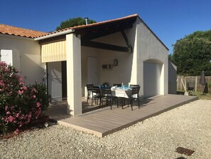 Eine überdachte Terrasse mit Tisch und Stühlen, eine Schotterauffahrt und ein Haus mit Ziegeldach.