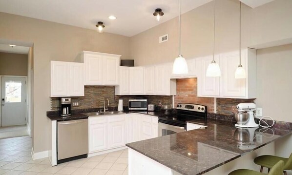 A modern kitchen with white cabinets, granite countertops, a large island, and pendant lighting. - Cozy Brick Home in Benton Park w/ parking (St. Louis)
