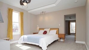 Een slaapkamer met een bed, nachtkastjes, een plafondventilator en een raam met gordijnen.